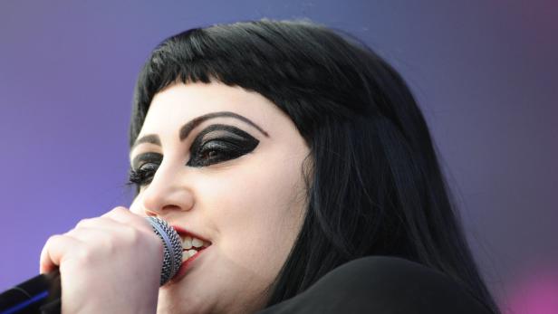 Eine Sängerin mit starkem Make-up singt in ein Mikrofon.