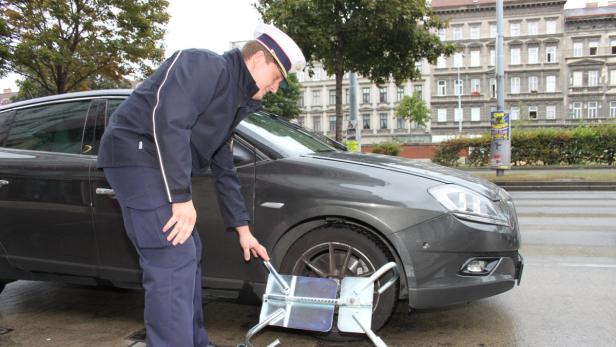 Ein Polizist befestigt eine Radkralle an einem grauen Auto.