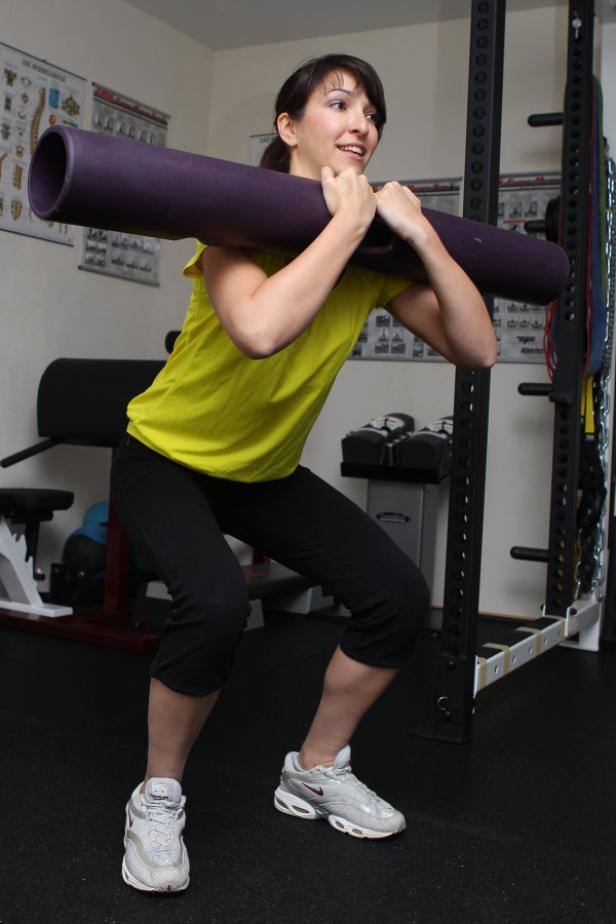 Eine Frau macht Kniebeugen mit einem Gewicht auf ihren Schultern in einem Fitnessstudio.