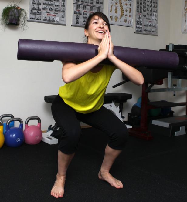 Eine Frau macht Kniebeugen mit einer Langhantel auf ihren Schultern in einem Fitnessstudio.