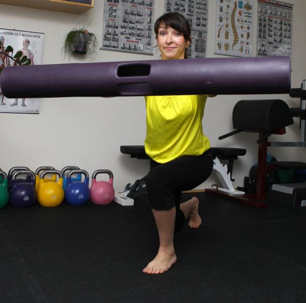 Eine Frau macht eine Ausfallübung mit einer Langhantel in einem Fitnessstudio.