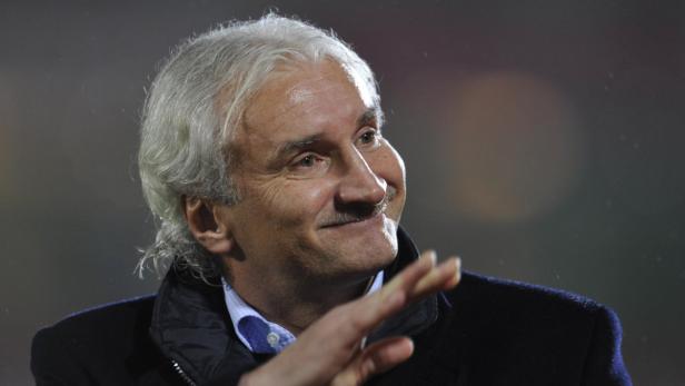 Ein älterer Mann mit grauem Haar lächelt und winkt.