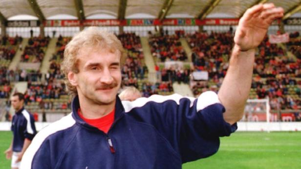 Ein Mann mit Schnurrbart winkt in einem Fußballstadion.