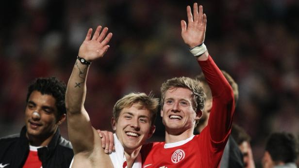 Zwei Fußballspieler umarmen sich und winken in die Menge.
