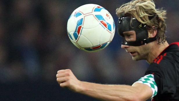 Ein Fußballspieler mit einer Gesichtsmaske köpft einen Ball.