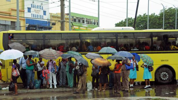 Menschen mit Regenschirmen warten bei Regen auf einen gelben Bus.