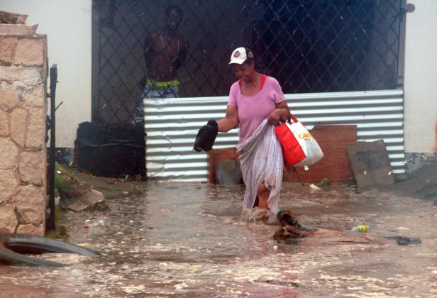 Eine Frau watet durch das knietiefe Hochwasser vor einem Haus.