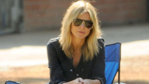 Eine blonde Frau mit Sonnenbrille sitzt auf einem blauen Stuhl.