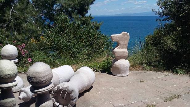 Große Schachfiguren aus Stein stehen auf einer Terrasse mit Blick auf das Meer.