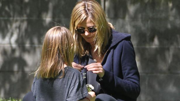 Eine Frau mit Sonnenbrille sitzt mit einem Kind im Gras und betrachtet Gänseblümchen.
