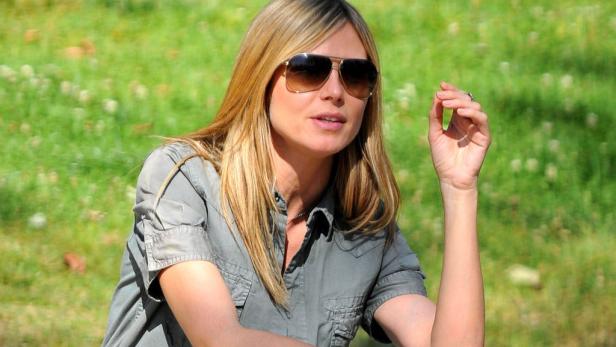 Heidi Klum sitzt im Grünen und trägt eine Sonnenbrille.