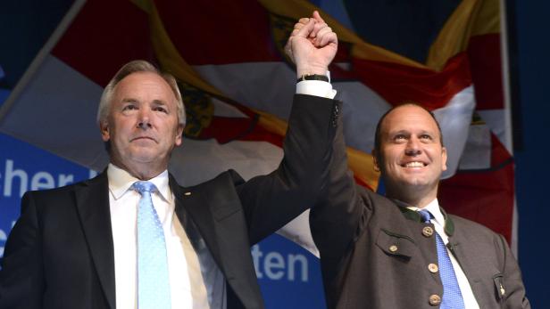 Zwei Männer stehen vor Flaggen und erheben die Arme.