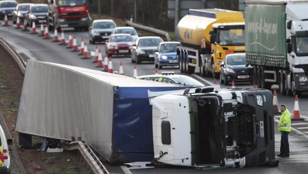 Ein umgekippter Lastwagen blockiert eine Autobahn, während andere Fahrzeuge warten.