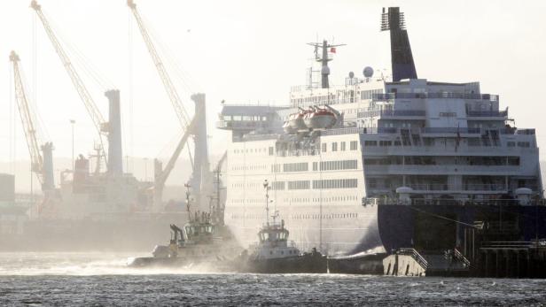Ein großes Kreuzfahrtschiff wird von zwei Schleppern in einen Hafen gezogen.