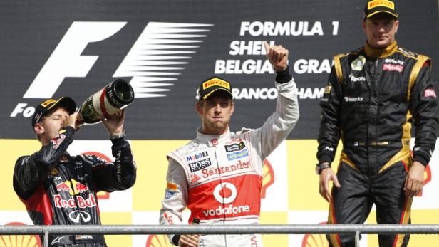Sebastian Vettel trinkt Champagner, während Jenson Button und Kimi Räikkönen auf dem Formel-1-Podium stehen.