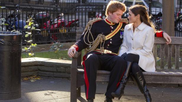 Prinz Harry in Uniform sitzt mit einer Frau auf einer Bank.