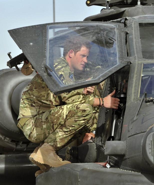 Prinz Harry in Militärkleidung hockt in einem Apache-Hubschrauber.