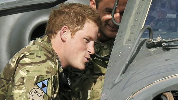 Prinz Harry in Militäruniform vor einem Hubschrauber, mit einem weiteren Soldaten im Hintergrund.