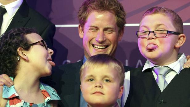 Prinz Harry posiert mit drei Kindern, die ihre Zungen herausstrecken.