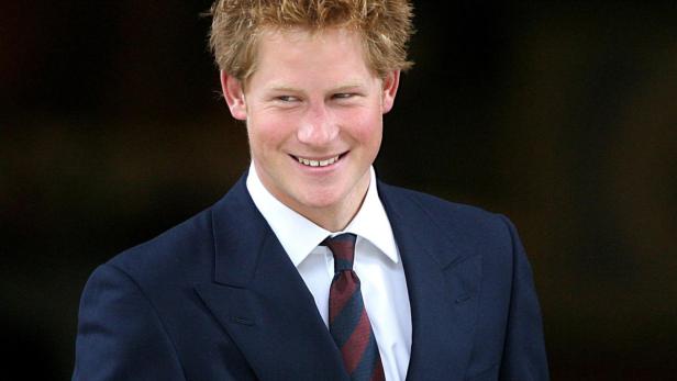 Prinz Harry lächelt in einem dunklen Anzug und einer gestreiften Krawatte.