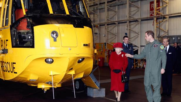 Königin Elisabeth II. besucht einen gelben RAF-Rettungshubschrauber in einer Halle.