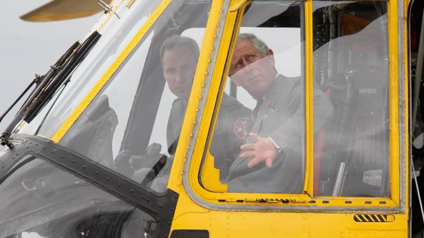 Prinz William und König Charles III. sitzen im Cockpit eines gelben Hubschraubers.
