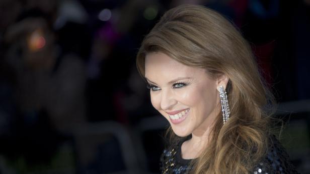 Kylie Minogue lächelt mit glitzerndem Ohrring und dunklem, paillettenbesetztem Oberteil.