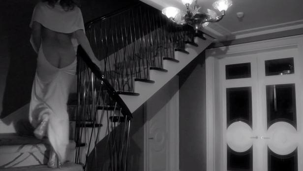 Eine Frau in einem weißen Kleid steigt eine Treppe in einem Haus hinauf.