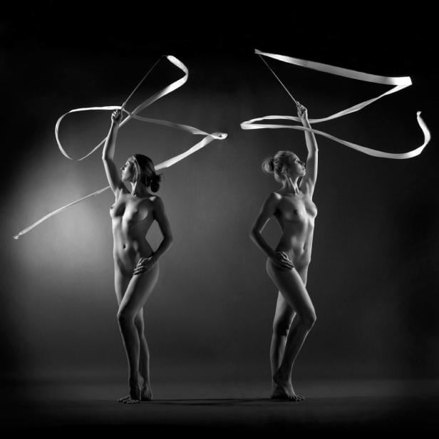 Zwei Frauen posieren mit Bändern für rhythmische Sportgymnastik vor einem dunklen Hintergrund.