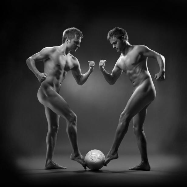 Zwei nackte Männer stehen sich gegenüber und spielen mit einem Fußball.