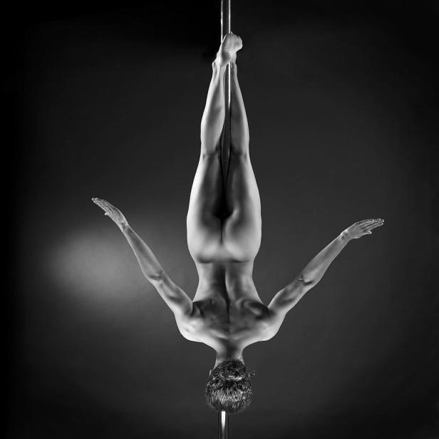 Eine Frau macht Pole Dance und hängt kopfüber an einer Stange.