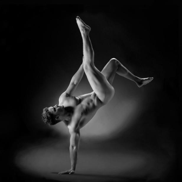 Ein Mann balanciert auf einer Hand, während er die Beine in der Luft verschränkt.