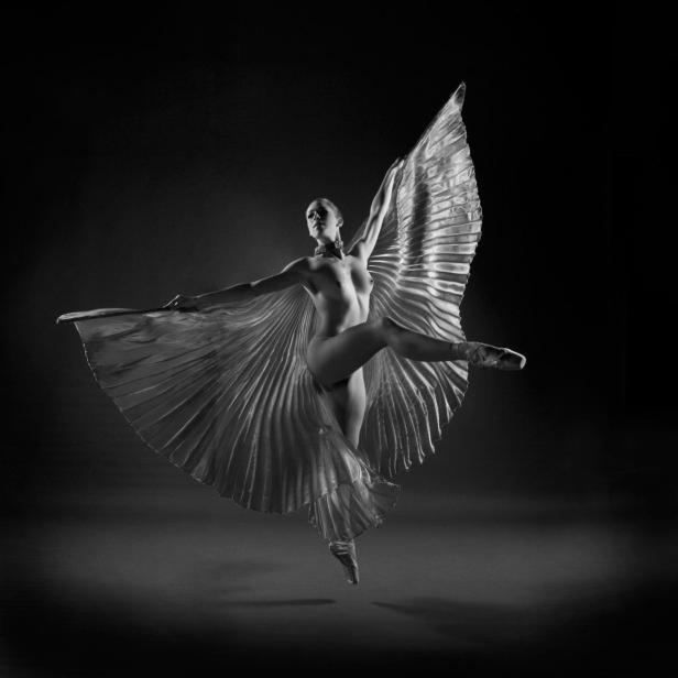 Eine Ballerina tanzt mit einem plissierten Stoff, der wie Flügel wirkt.