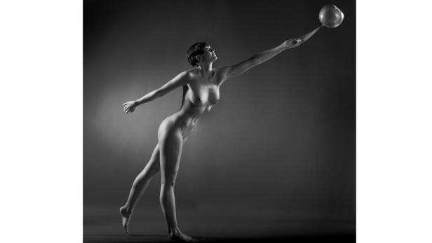 Eine nackte Frau in Bewegung berührt einen Ball mit einem Schläger.