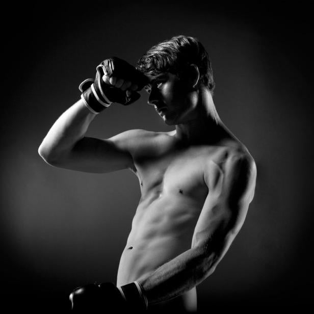 Ein muskulöser Mann mit Boxhandschuhen posiert vor dunklem Hintergrund.