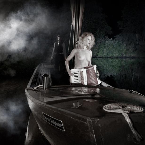 Eine Frau spielt Akkordeon auf einem Boot, während ein Mann im Hintergrund steht.