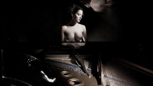 Eine Frau sitzt vor einem Klavier in einem dunklen Raum.