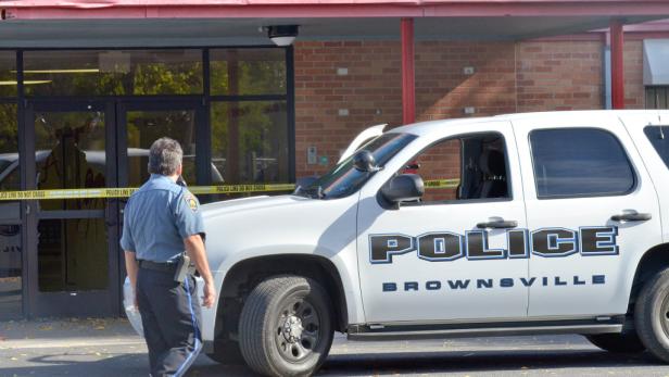Ein Polizist steht vor einem Gebäude mit zerbrochenen Fenstern und einem Polizeiwagen in Brownsville.