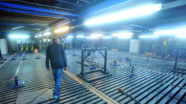 Ein Mann geht über einen Gitterboden in einer Industriehalle mit blauen Neonröhren.