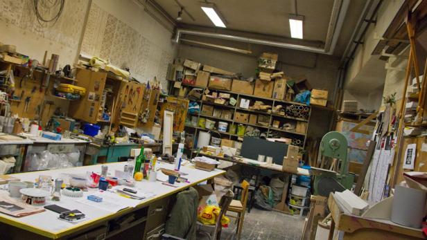 Ein chaotischer Werkraum mit Werkzeugen, Materialien und Regalen voller Kisten.