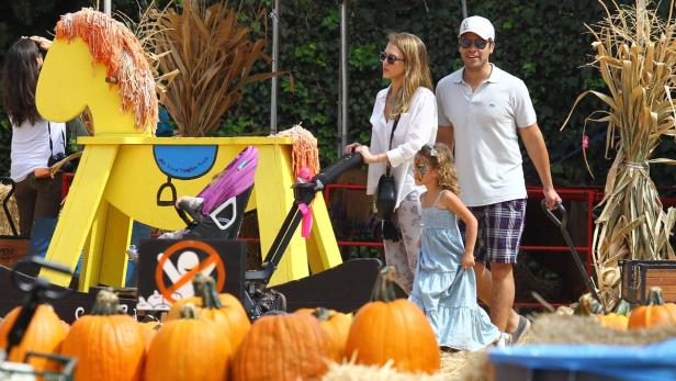 Eine Familie besucht einen Kürbishof mit einem gelben Holzpferd im Vordergrund.
