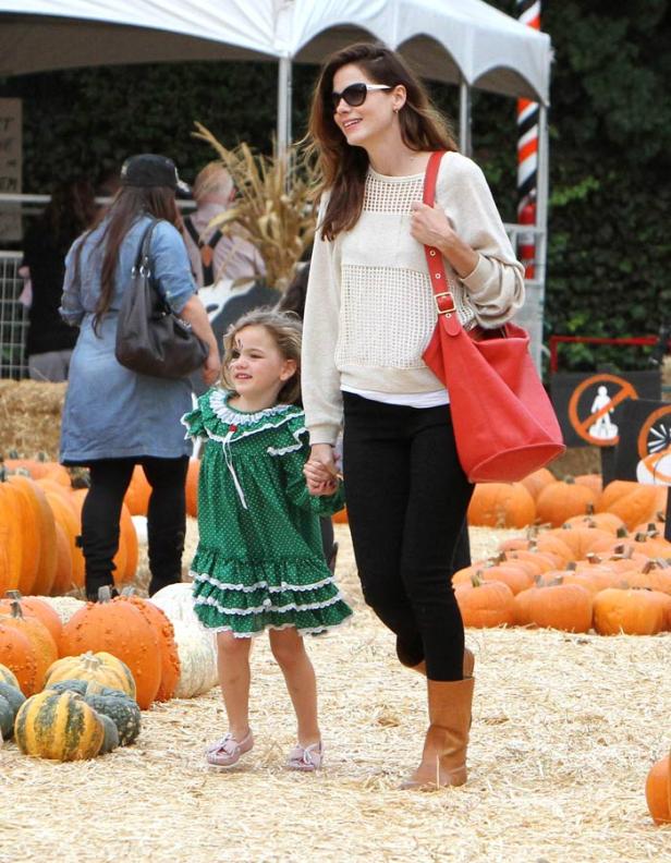 Eine Frau mit Sonnenbrille und ein kleines Mädchen halten Händchen auf einem Kürbisfeld.