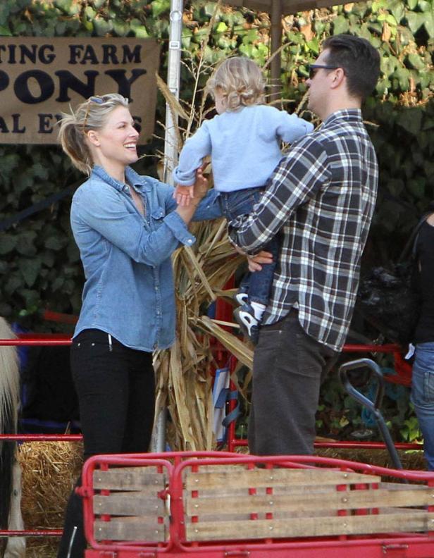 Eine Familie auf einem Ponyhof, wo der Vater ein Kind hält und die Mutter es anlächelt.