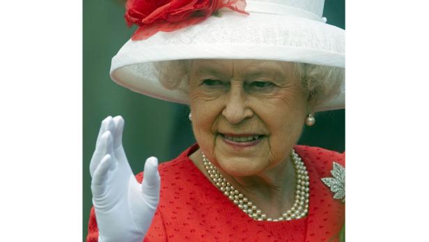 Königin Elisabeth II. mit einem weißen Hut und einem roten Kleid winkt.