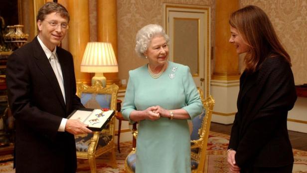 Bill Gates hält eine Auszeichnung vor Königin Elisabeth II. und einer weiteren Frau.