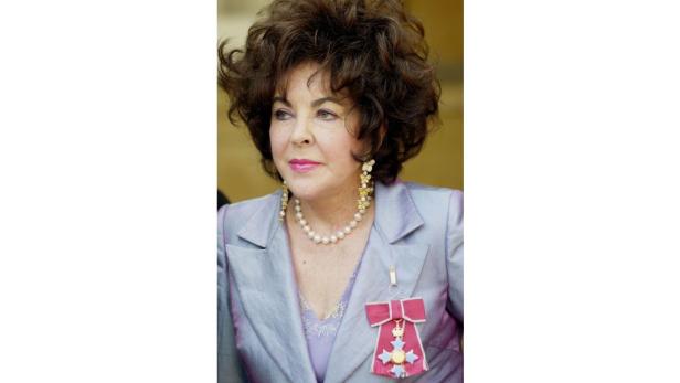 Elizabeth Taylor mit Perlenkette und einem Orden an einem hellblauen Blazer.