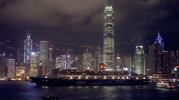Ein Kreuzfahrtschiff vor der Skyline von Hongkong bei Nacht.