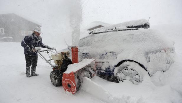Ein Mann räumt mit einer Schneefräse Schnee von einem Auto frei.