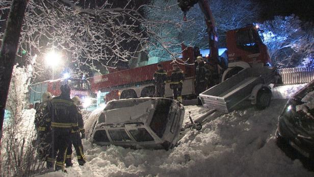 Ein auf dem Dach liegendes Auto wird von der Feuerwehr in einer verschneiten Nacht geborgen.