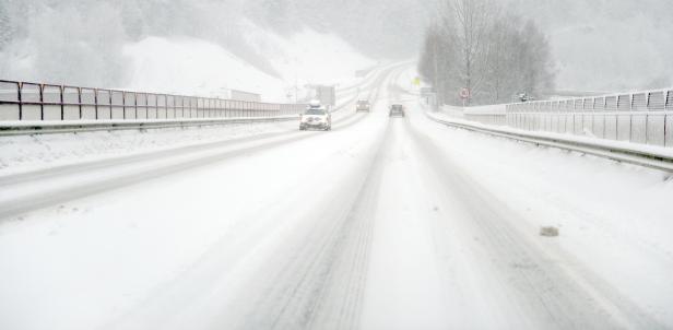 Autos fahren auf einer schneebedeckten Autobahn bei starkem Schneefall.